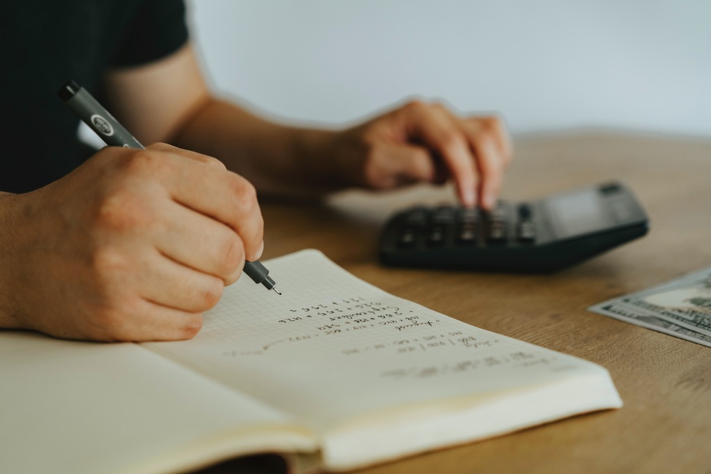 Pessoa escrevendo em caderno e usando calculadora, o que simboliza declaração imposto de renda 2023